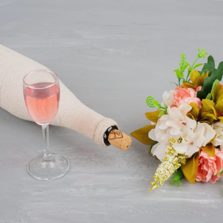a glass of rose wine with a wrapped bottle and a bouquet of pink roses