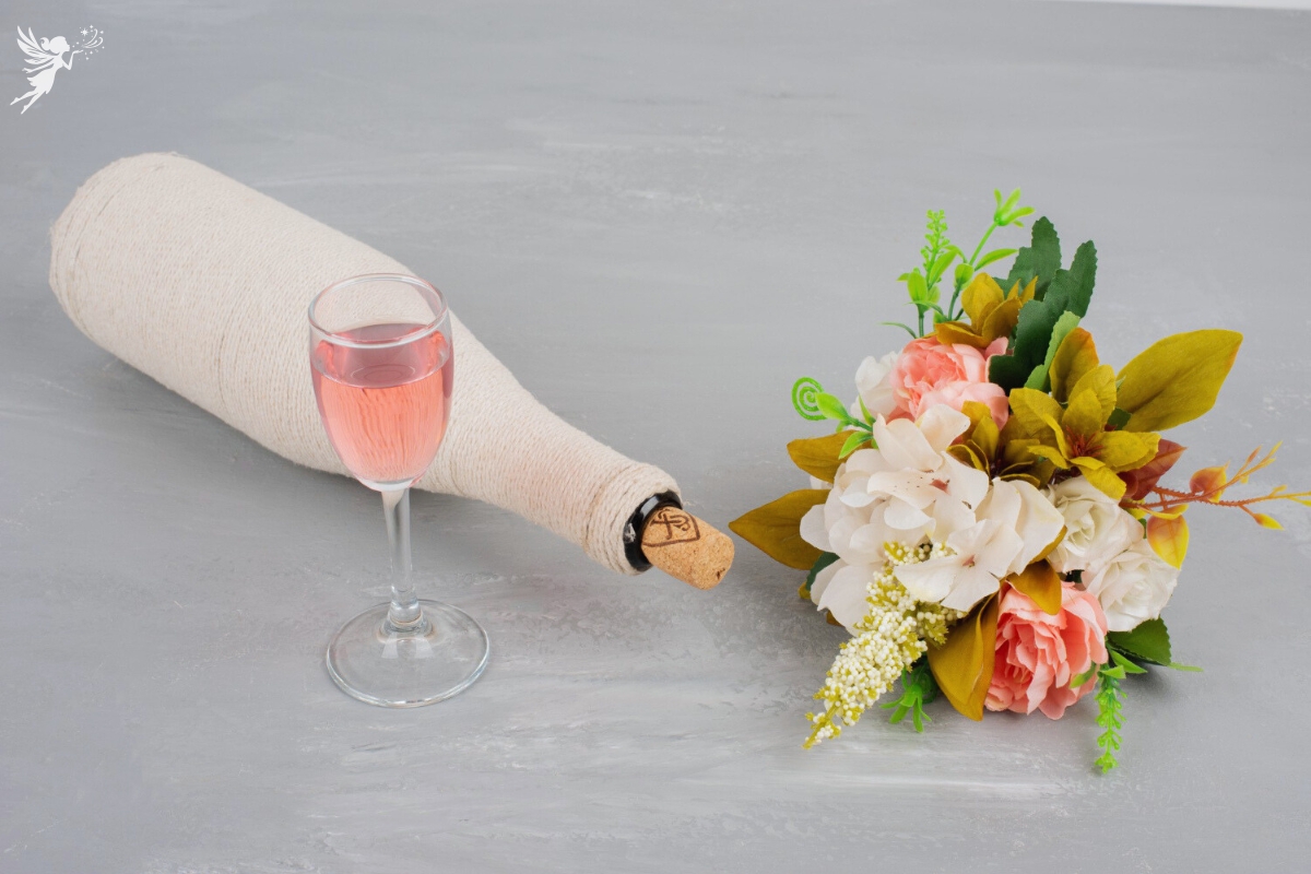 a glass of rose wine with a wrapped bottle and a bouquet of pink roses