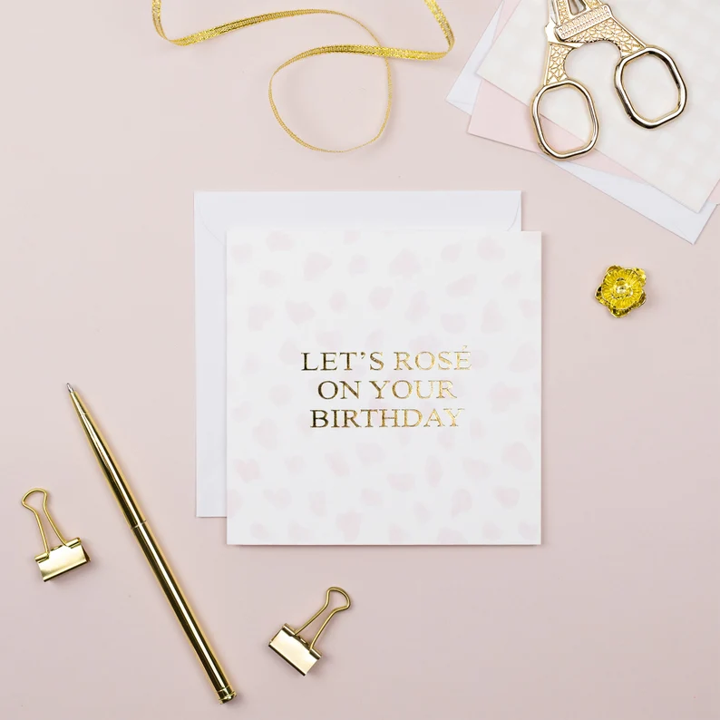 a card with gold foiled embossed writing Let's Rose on Your Birthday with a flatlay design