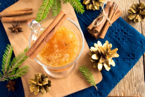 festive presentation of hot buttered rum glass with spruce and pines on blue cloth