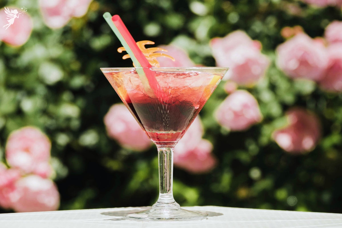 a red and pink colored cocktail against a background of roses in a garden