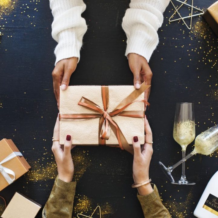 Hands exchanging wrapped gift with champagne, glasses, and festive decorations