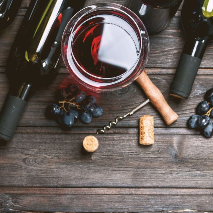 Red wine glass, bottles, corkscrew, and grapes on wooden table
