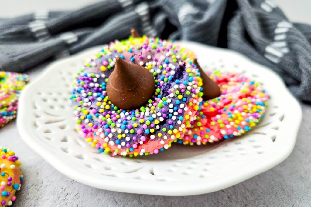 close up of a tie dye unicorn cookie on a white plate with a hersheys milk chocolate kiss on top