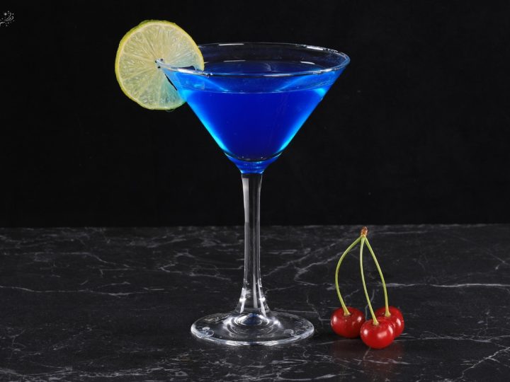a glass or blue martini with a slice of lemon dark background