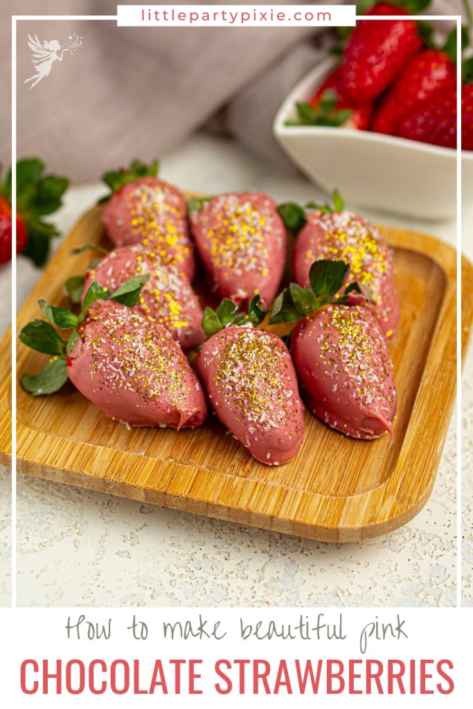 Pink chocolate-dipped strawberries with gold and white sprinkles arranged on a wooden tray for a party treat.