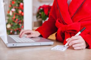 a lady in red dressing gown sitting at a laptop computer writing a wish list