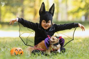a girl in bat costume with pet chihuahua in matching halloween costume
