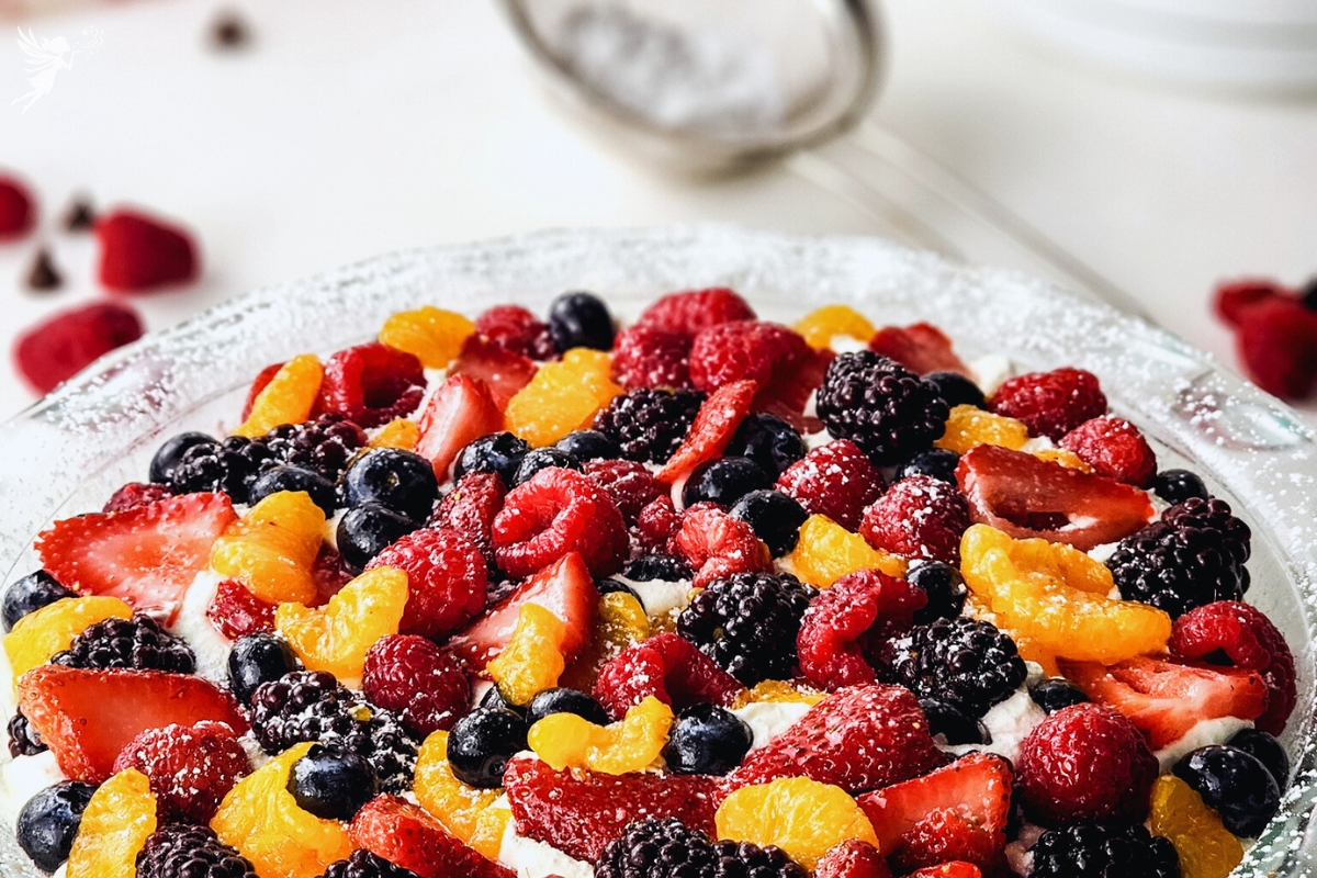 Colorful brownie fruit pizza topped with strawberries, blueberries, raspberries, blackberries, mandarin oranges, and powdered sugar.