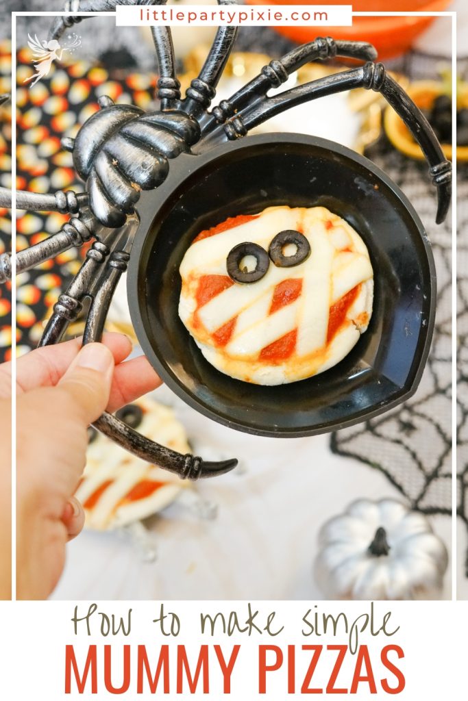 A spooky mummy pizza served in a black spider-shaped bowl, with stringy cheese and two sliced olive eyes.