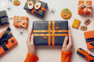 ladies hands holding a black and orange wrapped parcel with flat lay halloween decorations
