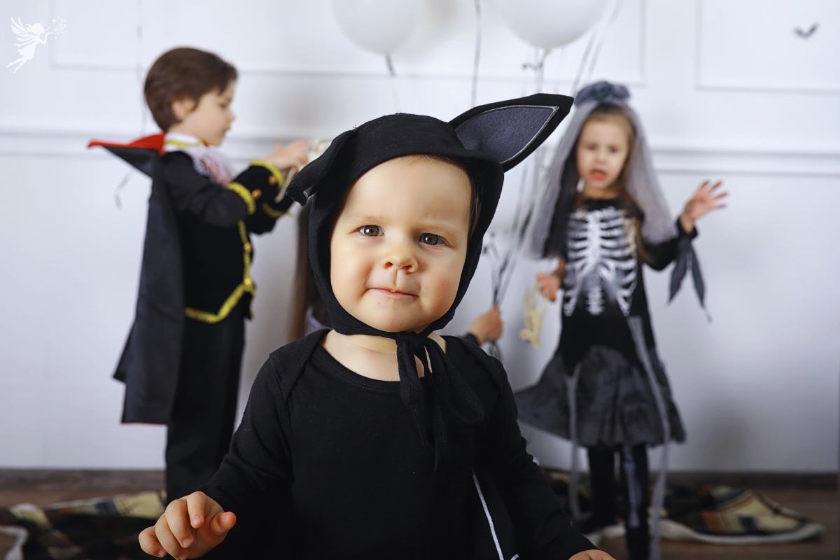 cute toddler wearing a cat halloween outfit with other toddlers in cute halloween outfits behind them