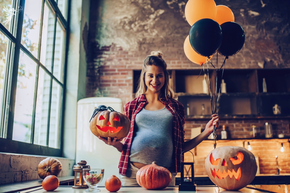 pregnant woman holding pumpkin and ornage and black balloons