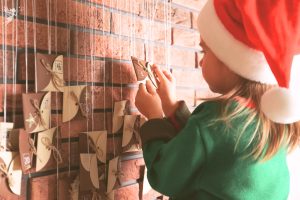 small child opening a little numbered envelop on a hanging advent calendar against brick wall