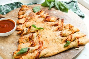 Baked Christmas Tree Pull-Apart Bread on a wooden board, garnished with basil and parmesan, served with dipping sauce.