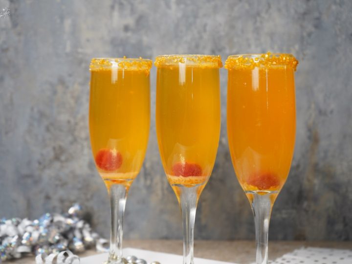 Three flutes of the vibrant Shimmering Golden Champagne Cocktail, garnished with a gold sugar rim and a cherry.
