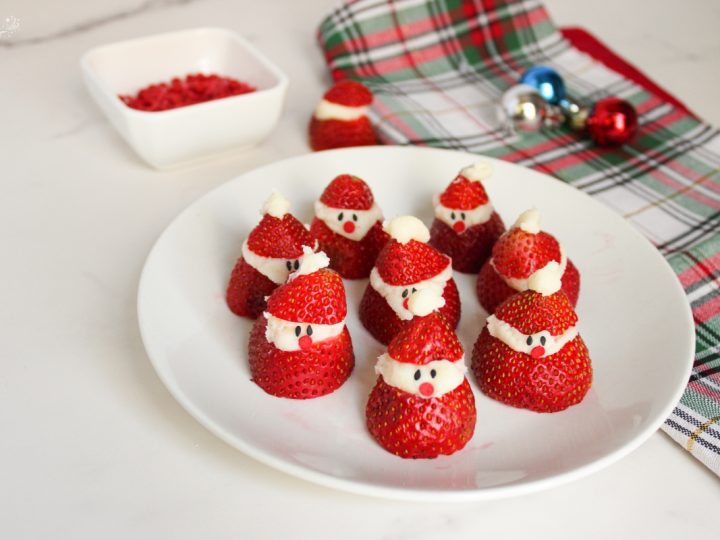 A handful of adorable Strawberry Santas standing upright, featuring sweet cream beards, button eyes, and mini chocolate chips.