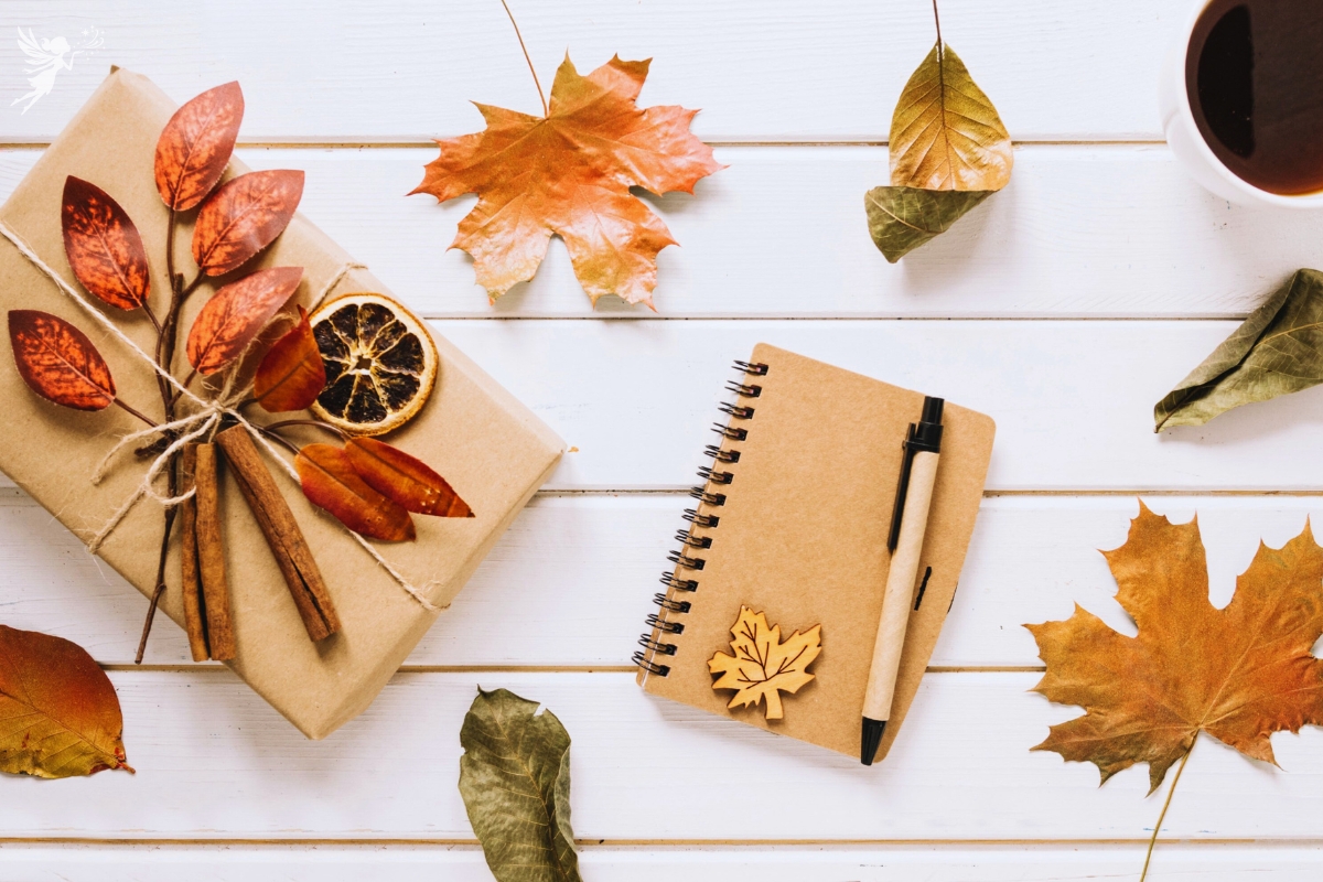 flat lay of a gift and notepad with a fall leaves setting on white wood background to display preparing a halloween hostess gift