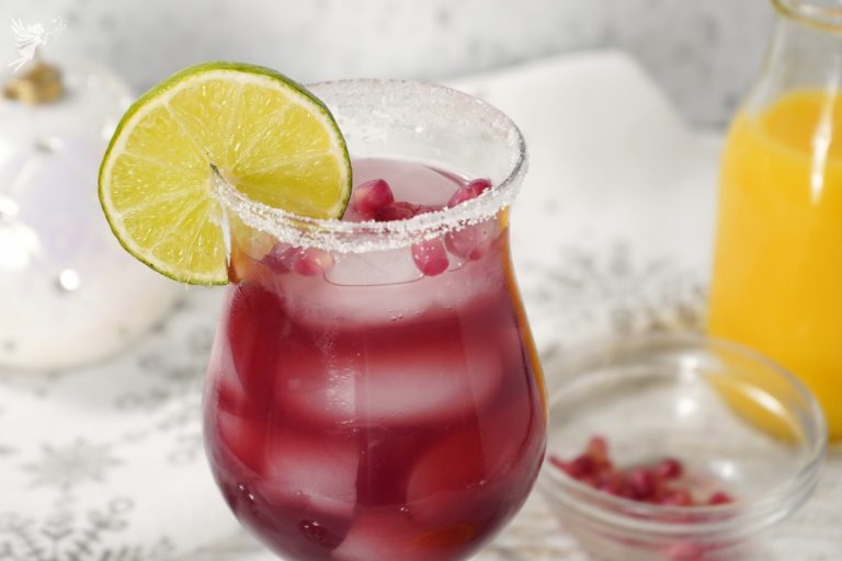 A chilled Pomegranate Margarita in a sugar-rimmed glass, showing the bright red cocktail with ice and a lime wheel.