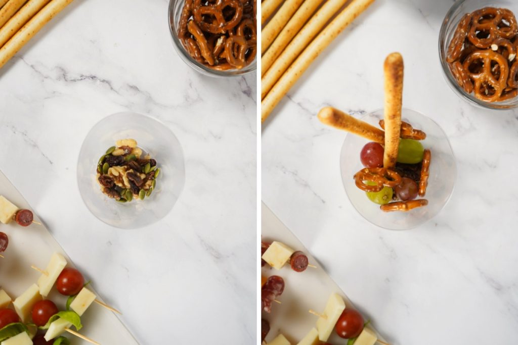Layering nuts, pretzels, grapes, and breadsticks in small cups to assemble individual charcuterie appetizer cups.