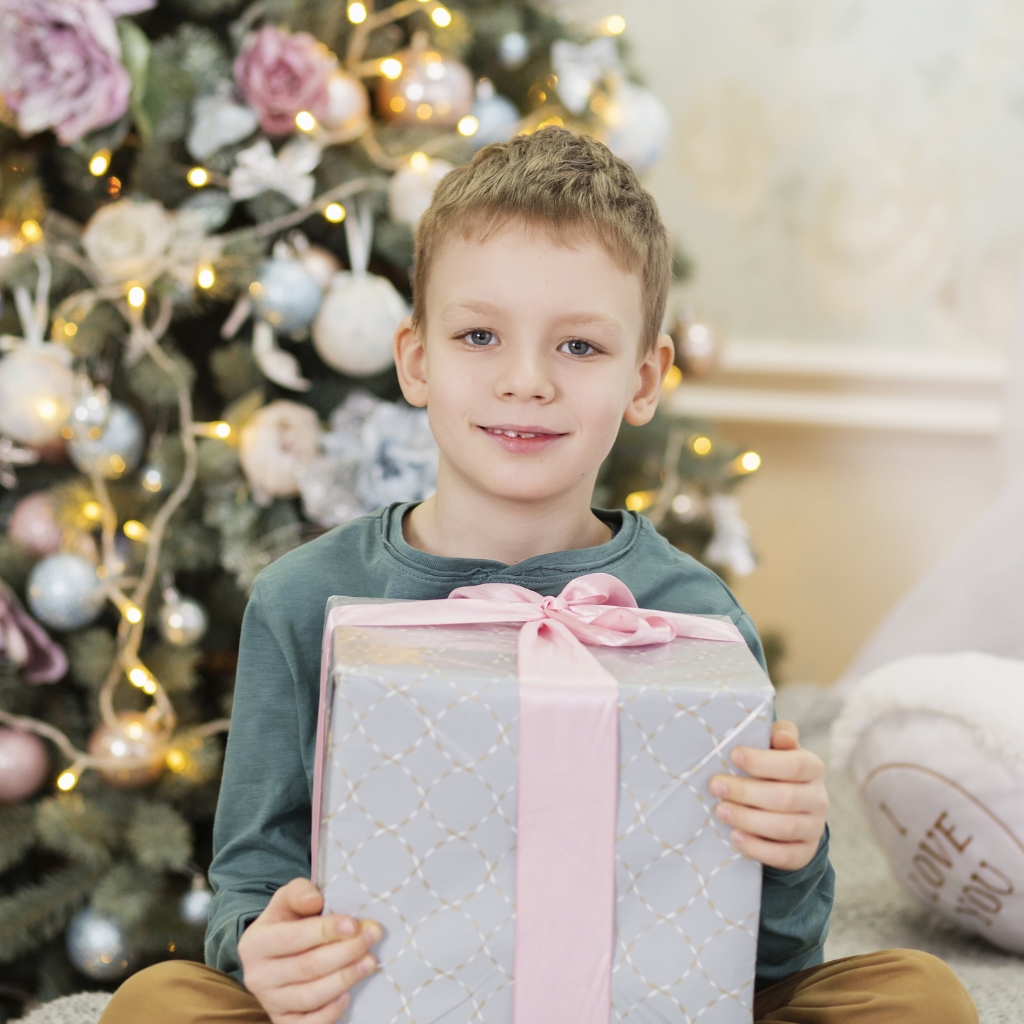 small boy holiding a pink present under a pastel decorated christmas tree