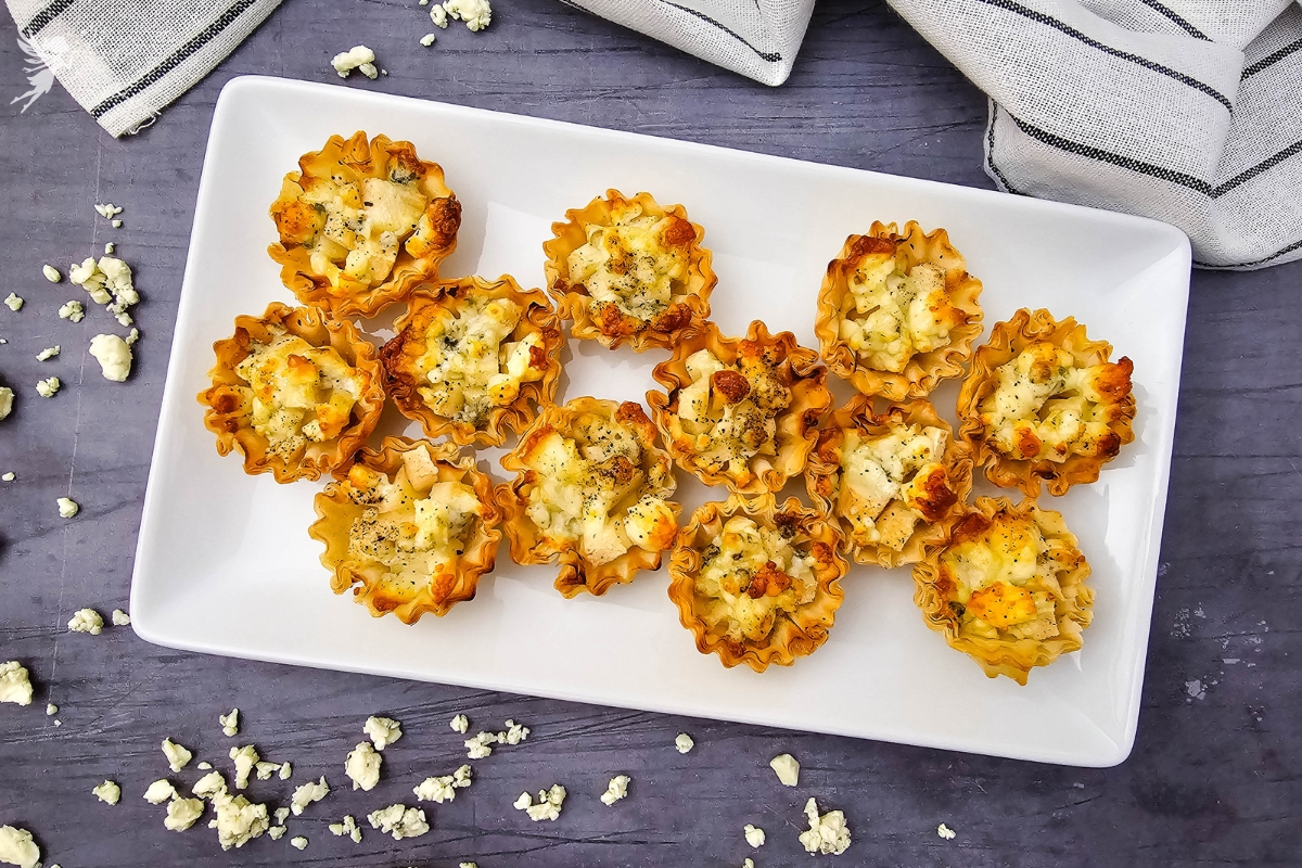 Crispy and elegant Blue Cheese & Pear Phyllo Bites arranged on a white platter with crumbled blue cheese.