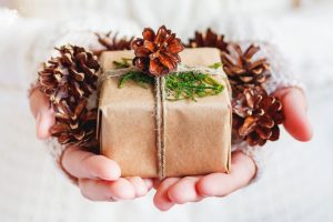 small christmas gift with brown paper and pine cones being held in a ladies hands white jumper