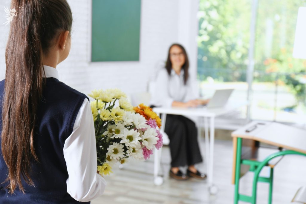 school girl approaching teacher with a bunch of flowers
