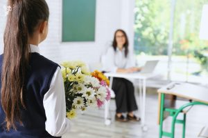 school girl approaching teacher with a bunch of flowers