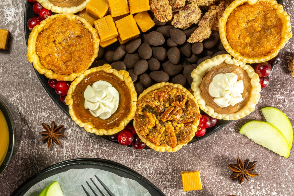 An elegant Mini Pie Dessert Platter featuring various mini pies, candies, candied nuts, and fresh cranberries.