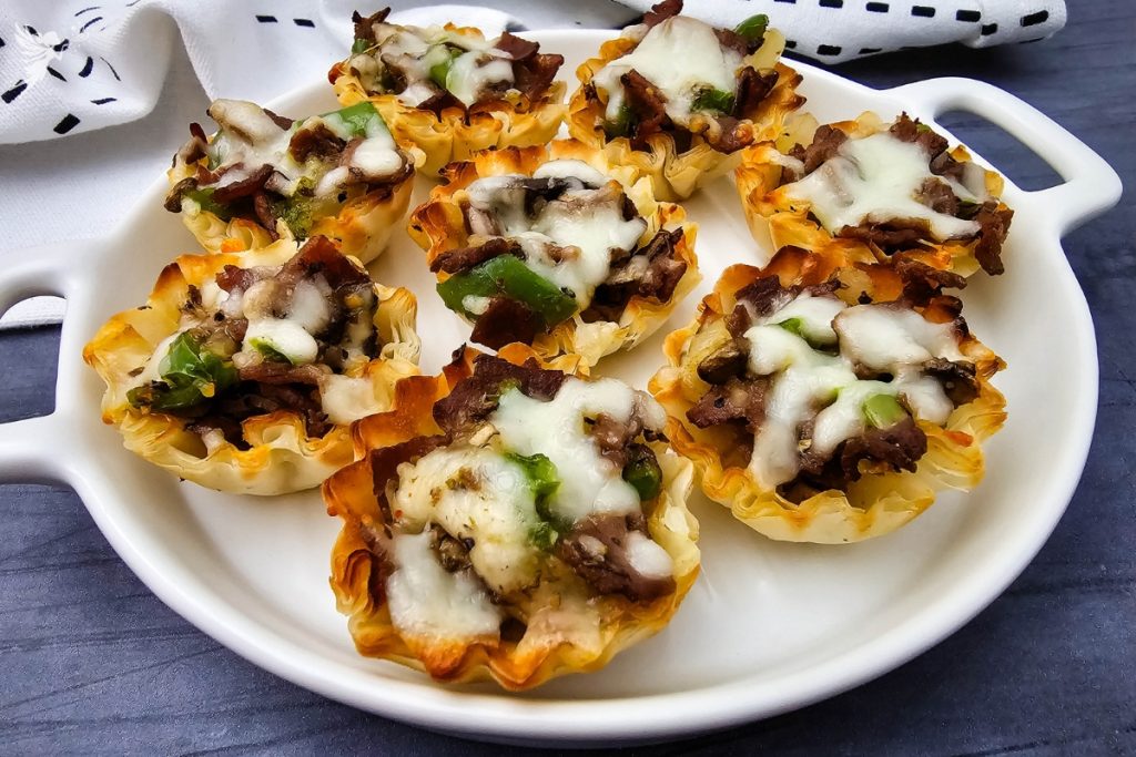 A close-up of several crispy Philly Cheesesteak Phyllo Bites served on a white appetizer plate.
