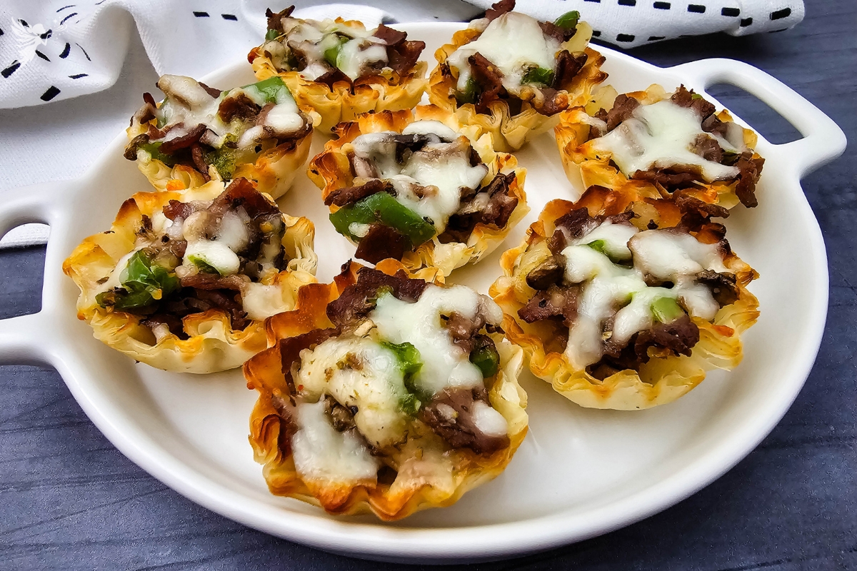 A close-up of several crispy Philly Cheesesteak Phyllo Bites served on a white appetizer plate.