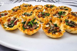 Close-up of multiple finished and delicious Stuffed Mushroom Phyllo Bites arranged neatly on a crisp white serving platter.