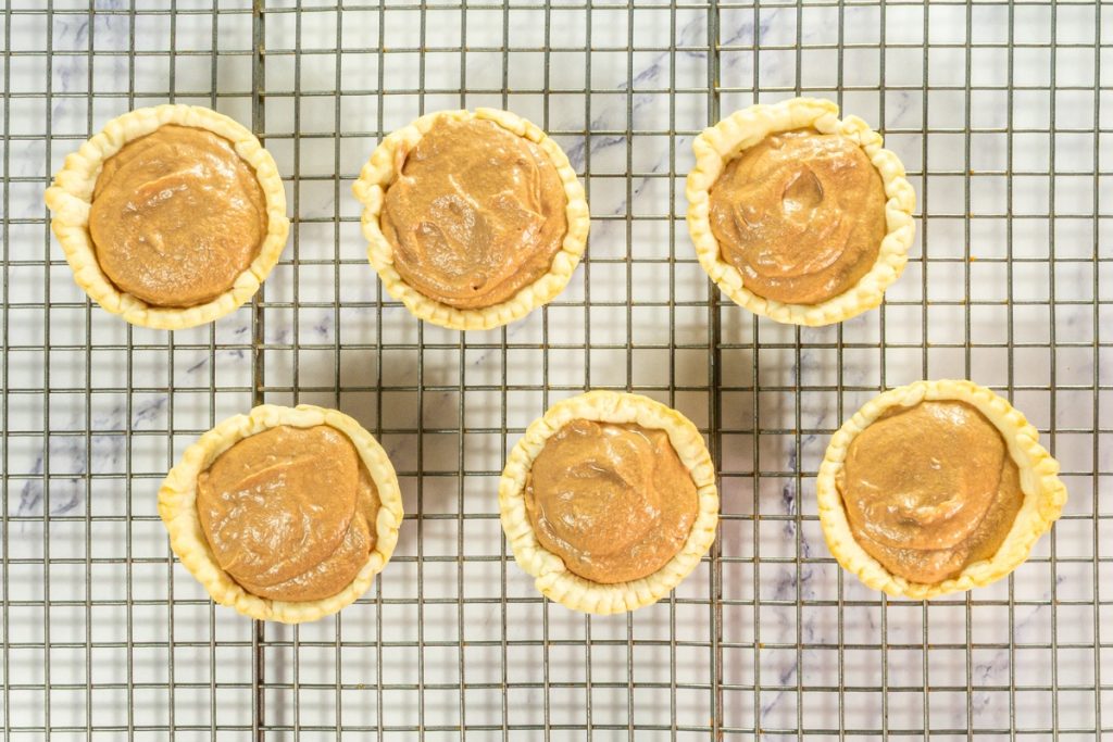 Six baked mini pie shells filled with smooth chocolate silk mixture cooling on a wire rack for the Chocolate Silk Pie that is part of Mini Pie Dessert Platter.