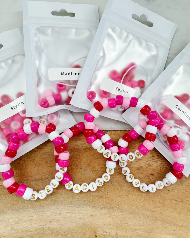 Customized pink and white pony bead friendship bracelets, spelling out names like "Stella" and "Taylor," packaged as Valentine's Day Party Favors. Etsy