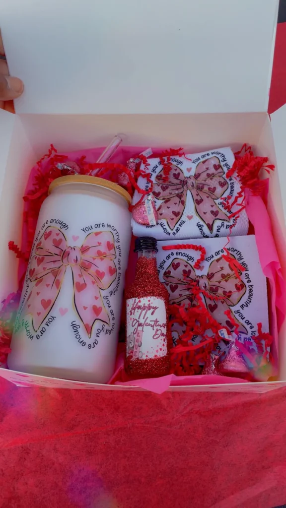 Festive Galentine's Day Gift Box containing a bow-themed glass tumbler, matching socks, and a small glittery bottle. Etsy