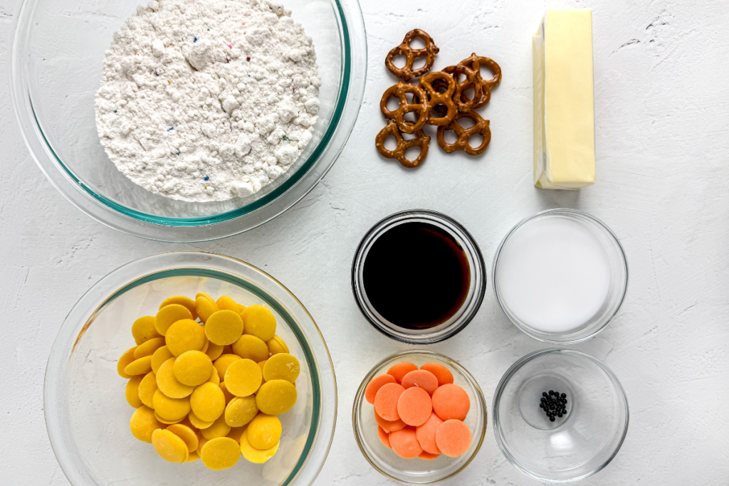 Overhead view of all ingredients for the Baby Chick Funfetti Truffles, including funfetti mix, butter, pretzels, and yellow and orange candy melts.