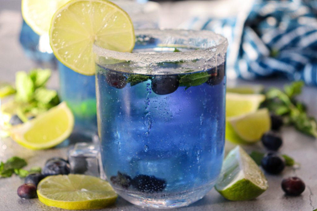 Close-up of the finished, sparkling blue Blueberry Mojito Mocktail in a sugar-rimmed glass, garnished with a fresh lime wheel.