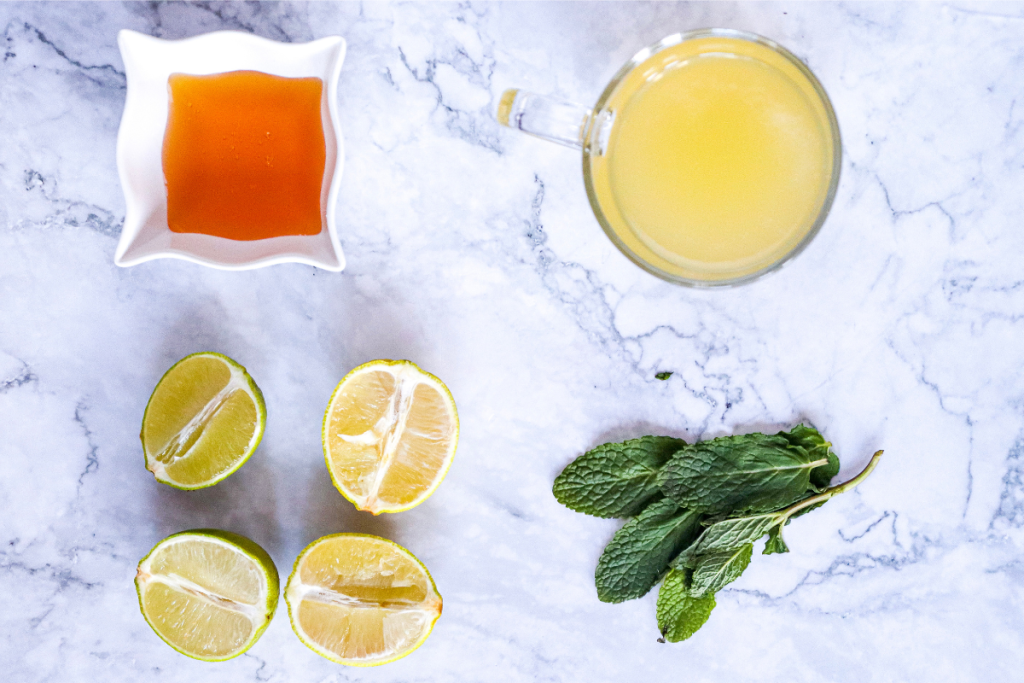 Ingredients laid out for the Classic Virgin Mojito Mocktail: fresh lime juice, lime halves, mint sprigs, and agave syrup.