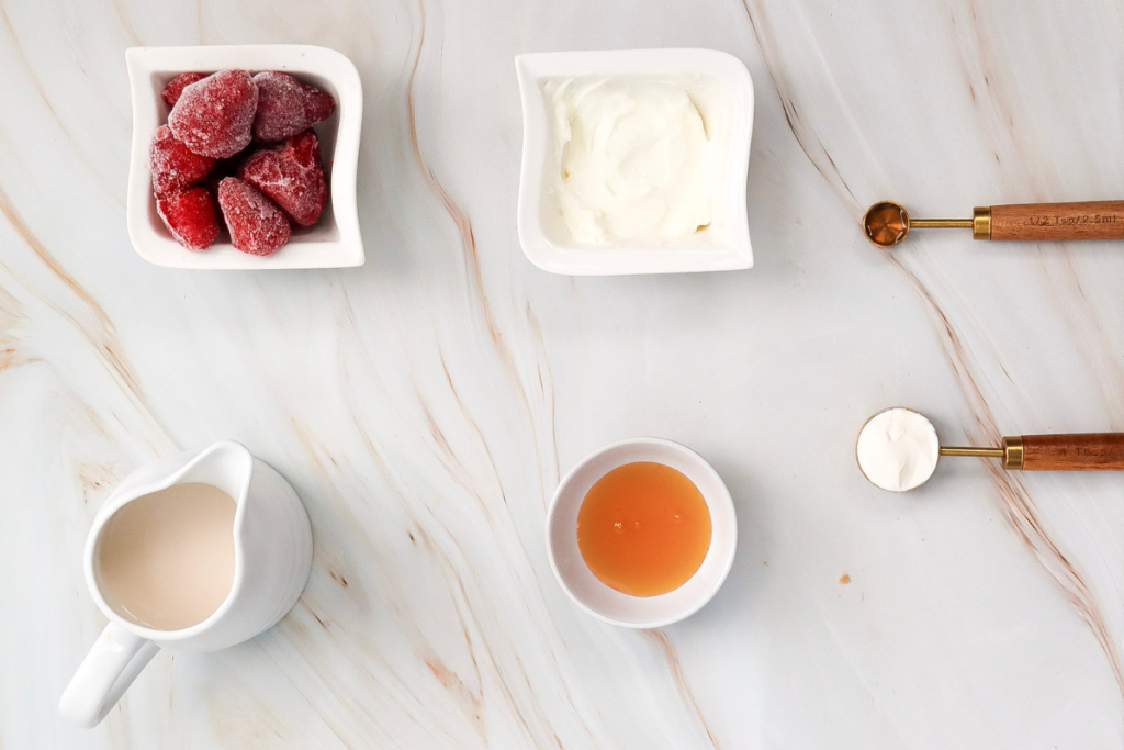Overhead shot of all ingredients, including frozen strawberries and cream cheese, needed for a homemade Strawberry Cheesecake Frappuccino.