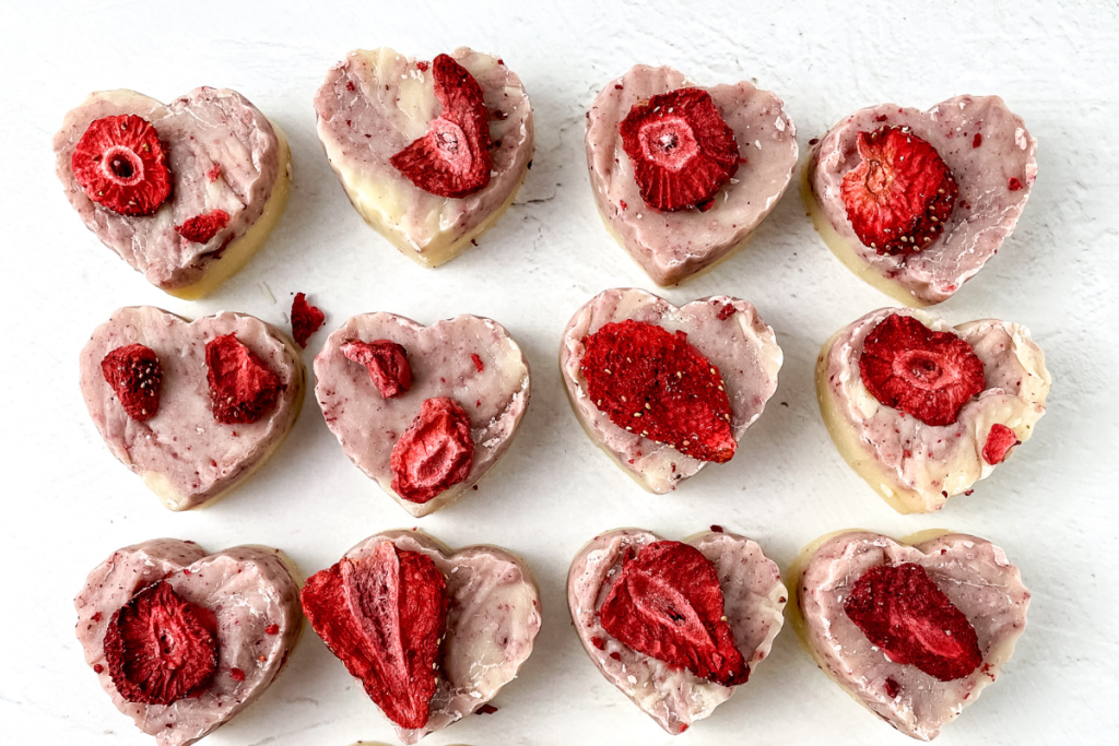 A dozen finished, heart-shaped pieces of marbled pink and white Strawberry Cream Fudge, each adorned with a piece of freeze-dried strawberry.