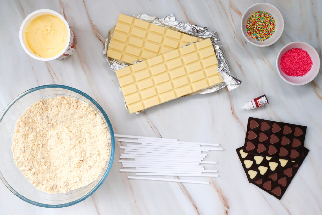 Ingredients are laid out, including cake mix, chocolate, frosting, and sticks, ready to create the delicious Valentine's Cake Pops.