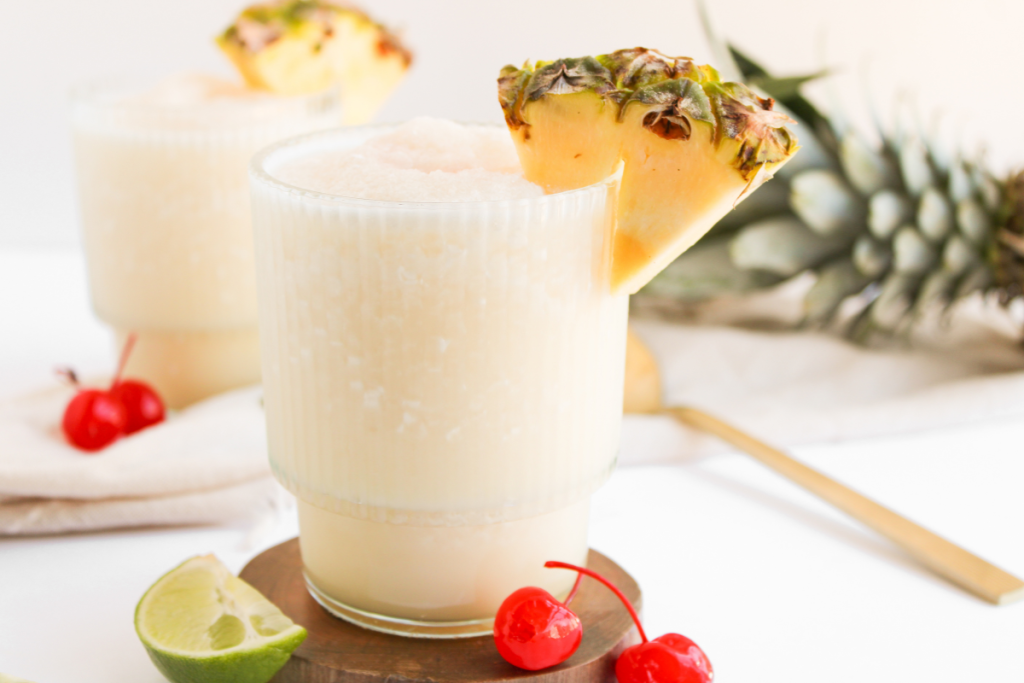 A finished, frosted Virgin Piña Colada served in a glass and garnished with a pineapple wedge and red maraschino cherries.