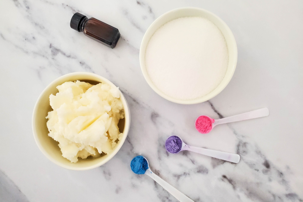 Solid coconut oil, white sugar, essential oil, and colorful mica powder in pink, purple, and blue are the ingredients for the Whipped Rainbow Sugar Scrub.