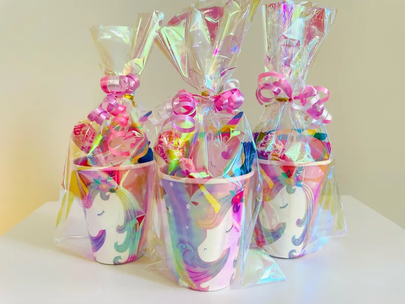 Three holographic cups pre-filled with treats and wrapped in clear iridescent plastic with pink bows, charming Unicorn Party Favors. Etsy