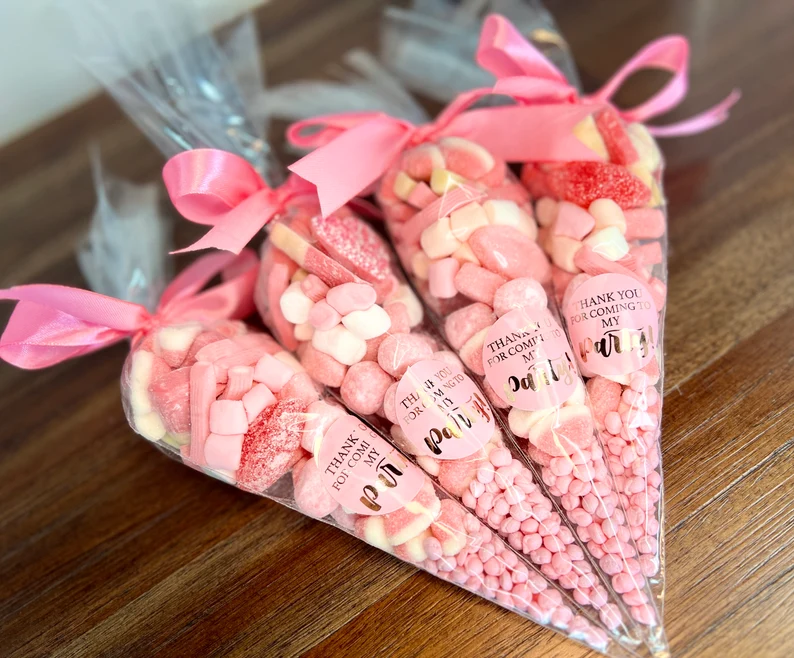 Four cellophane cone bags tied with pink ribbons, filled with various pink and white candies, labeled "THANK YOU," as ready-made Valentine's Day Party Favors. Etsy