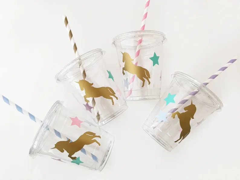Four clear plastic cups decorated with golden unicorn decals and colorful stars, each with a striped straw, excellent Unicorn Party Favors. Etsy