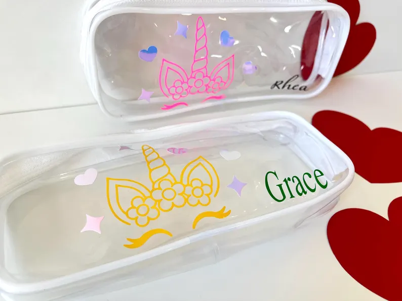 Two personalized, clear pencil/makeup pouches featuring colorful unicorn face decals and names, great as Unicorn Party Favors. Etsy