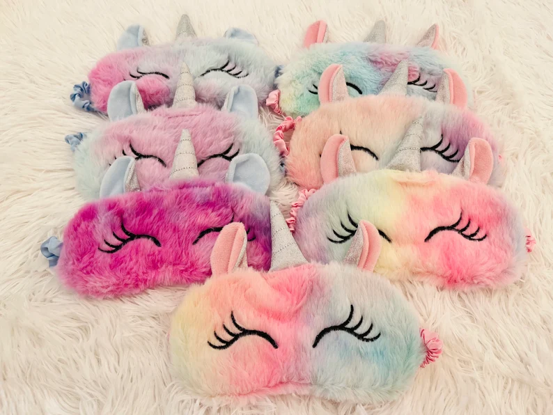 Seven soft, fluffy unicorn sleep masks in rainbow and pastel colors, featuring horns and eyelashes, perfect Unicorn Party Favors. Etsy