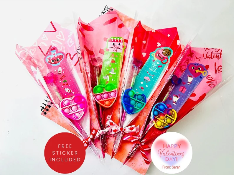 Four cellophane-wrapped Valentine's Day Party Favors bouquets featuring pencils, rulers with character heads, and heart-shaped pop-it fidget toys. Etsy